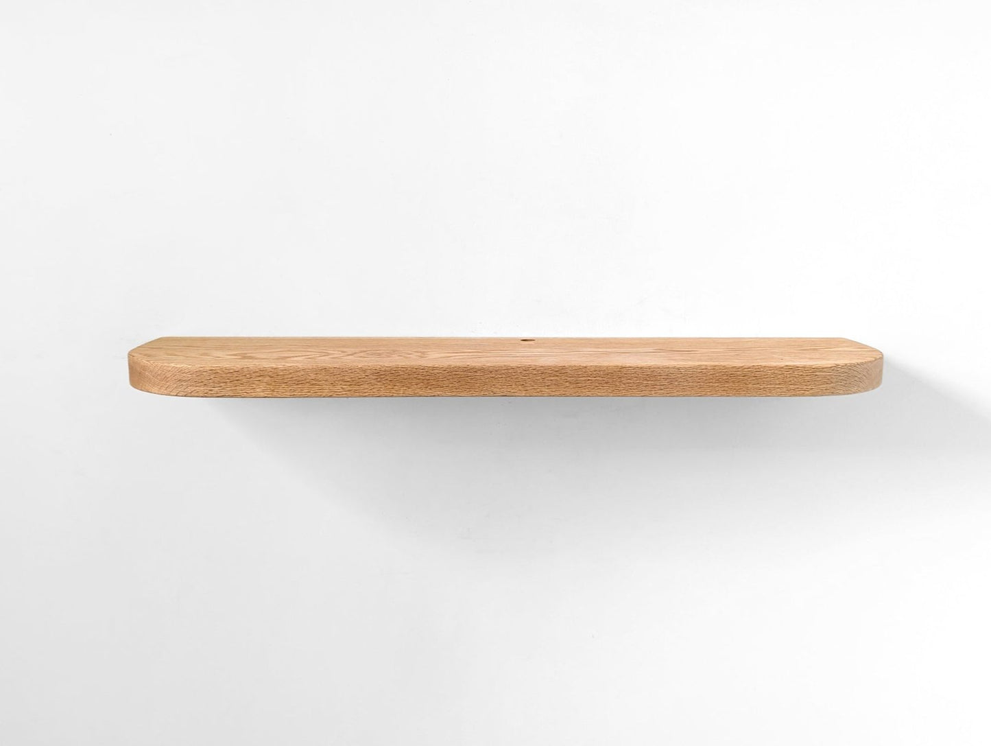 Straight photo of a thick oak floating shelf with curved edges and a cord hole