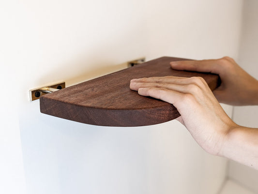Two hands push a mahogany floating shelf with curved corners onto two metal brackets