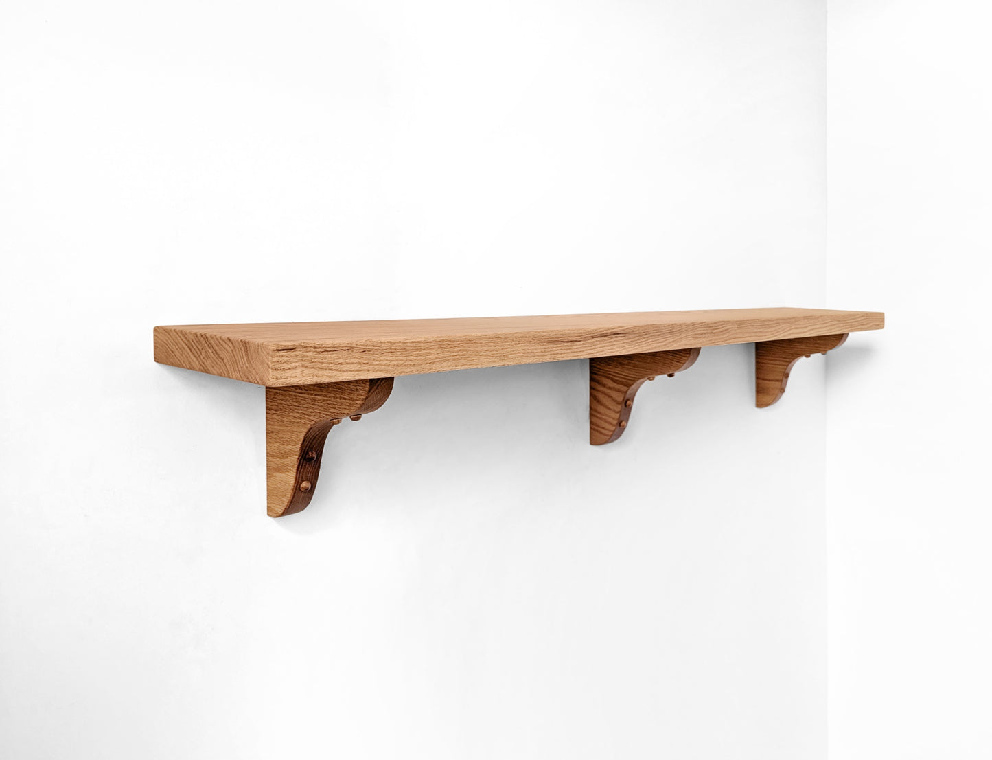 An oak floating shelf with three oak wooden brackets installed on a wall.