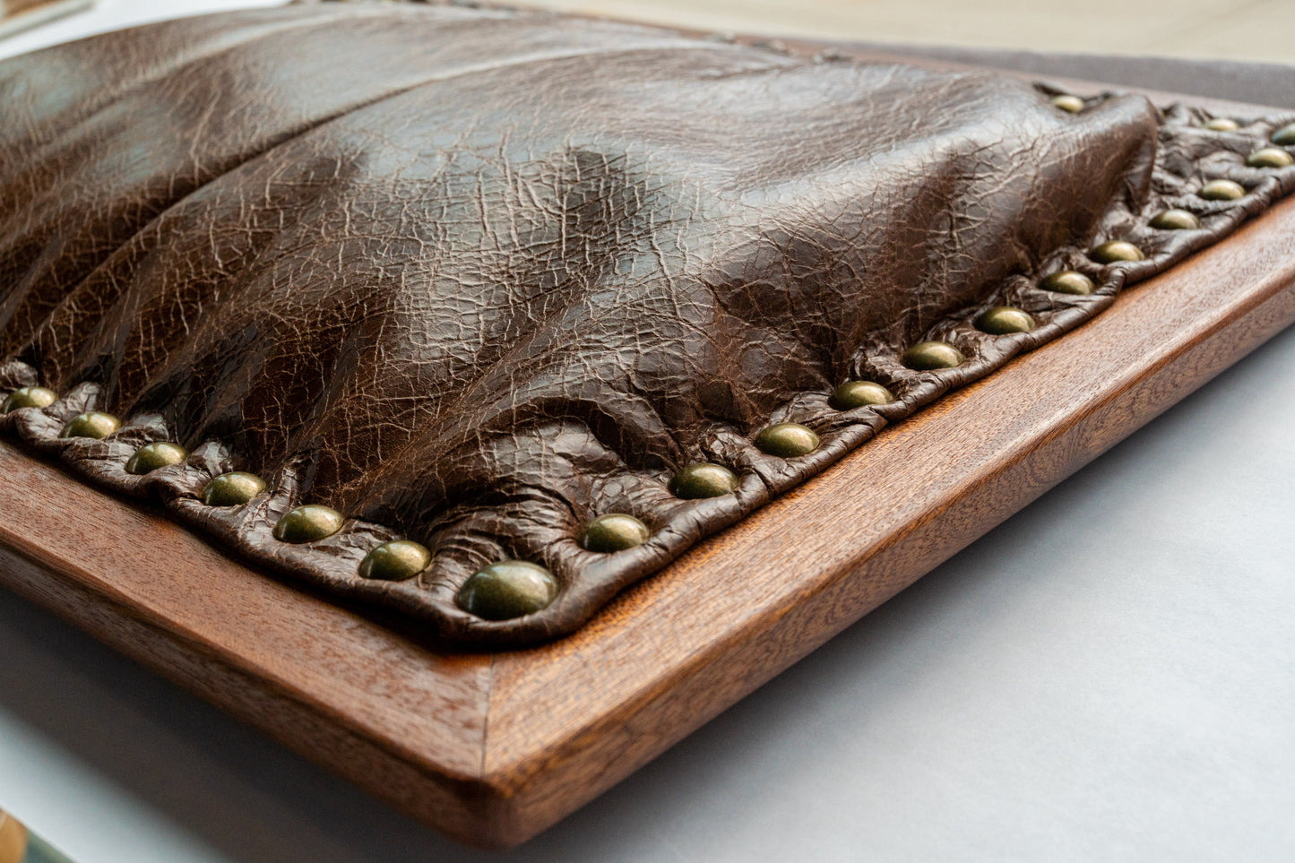 A side-view of our dark brown leather cushion writing lap desk. The grain of the dark brown leather is textured. The cushion protrudes from the solid mahogany frame and is stuffed with premium filling. Round brass pins secure the leather cushion to the wood frame.