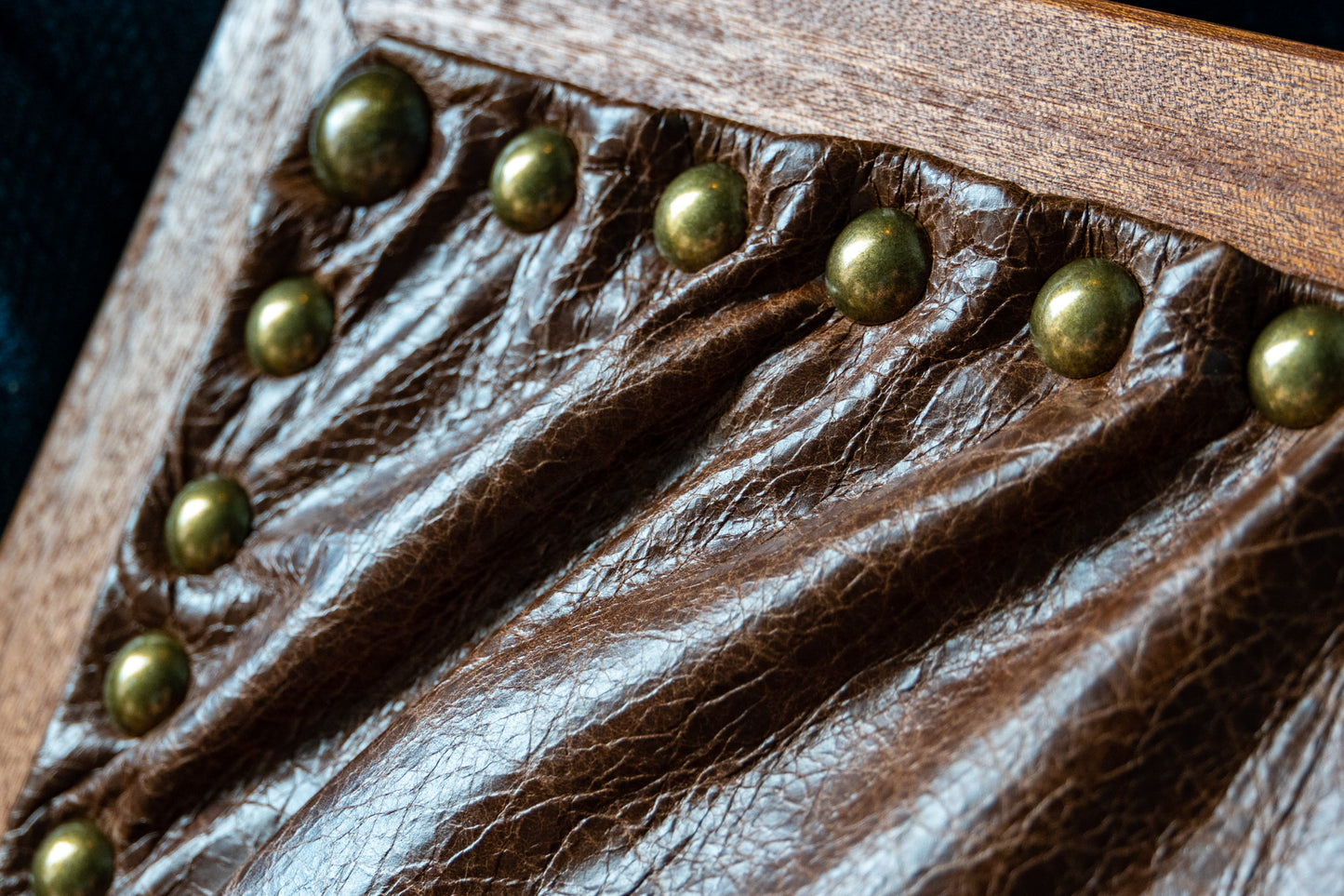 A close-up of the leather underbelly of our Leather Cushion Writing Lap Desk. The dark-brown leather appears soft and supple with small artery-like marks that add interesting texture. The leather cushion is attached by 10 brass round pins and is framed by solid mahogany wood. 