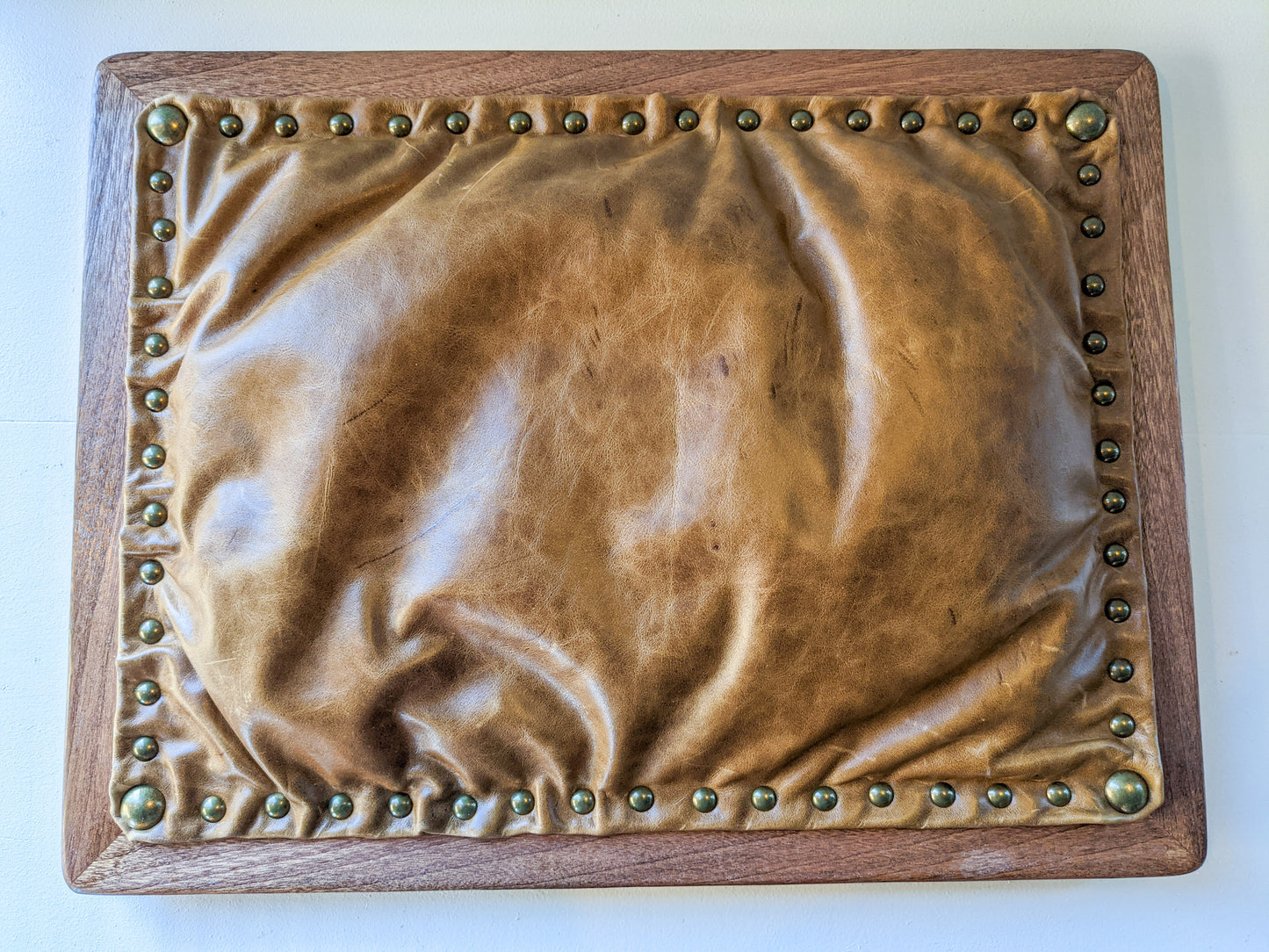 The bottom of our Leather Cushion Writing Lap Desk is shown. The mahogany wood frames a bulging bean filled, lightbrown, leather cushion that is securely attached by 56 shining brass pins.