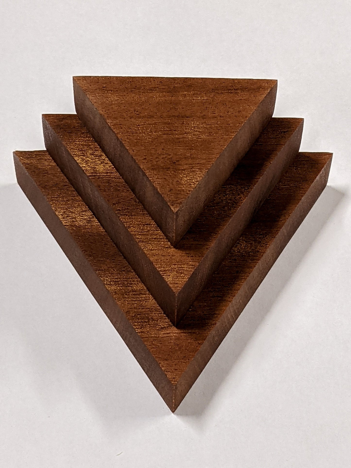 Three triangle floating shelves in mahogany sit on top of the other in varying sizes from largest to smallest.