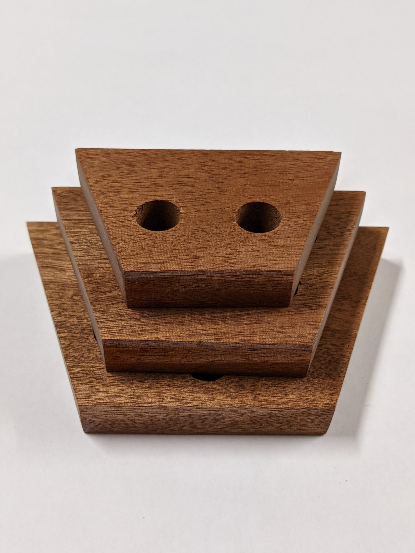 A set of three trapezoid mahogany propagation shelves sit one on top of the other with the largest at the bottom and the smallest on top.