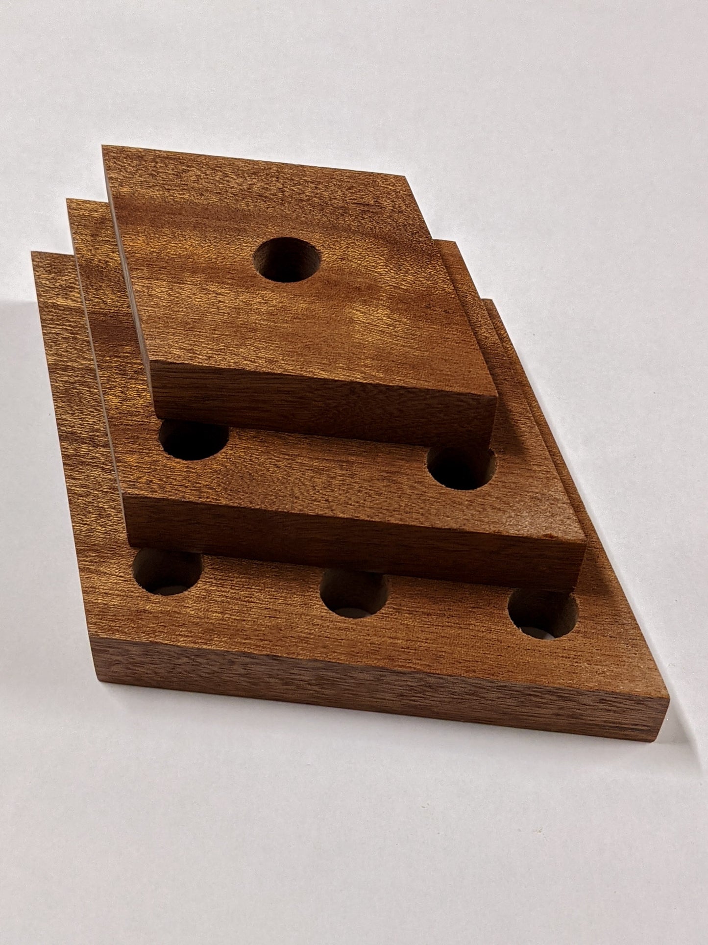 A set of three rhombus mahogany propagation shelves sit one on top of the other with the largest at the bottom and the smallest on top.