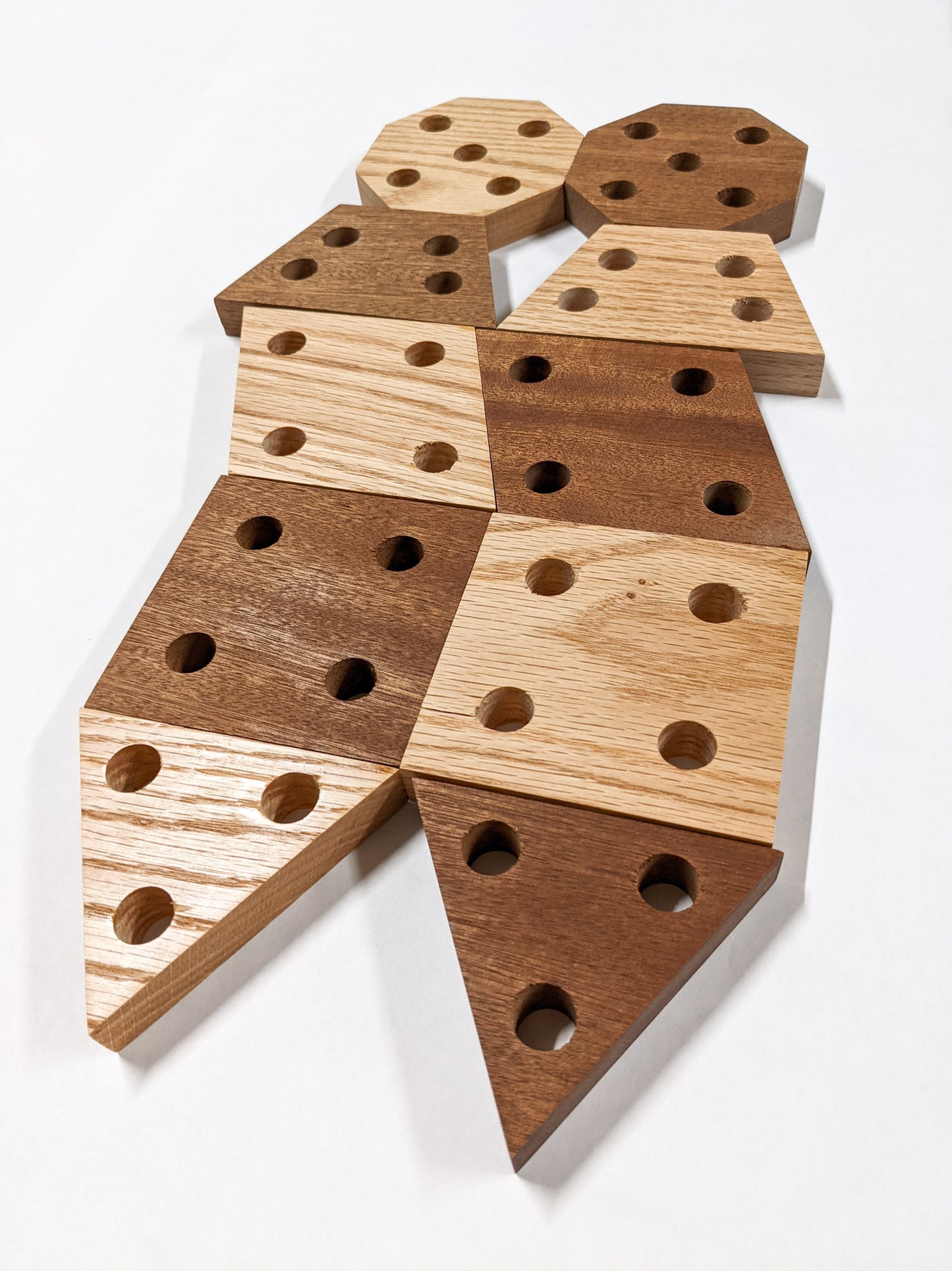 Each of the geometric propagation shelves is represented in oak and mahogany with four holes. From top to bottom, octagon, rhombus, trapezoid, square, and triangle. The triangle has three holes.
