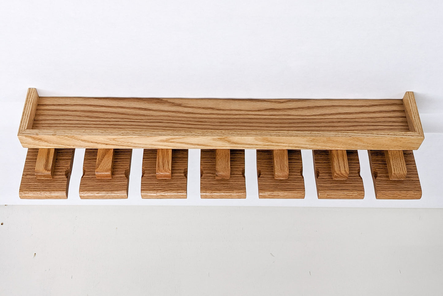 An empty beer glass shelf on a white background. The oak shelf has a small and long top with a raised edge while seven slats below allow for easy glass hanging.