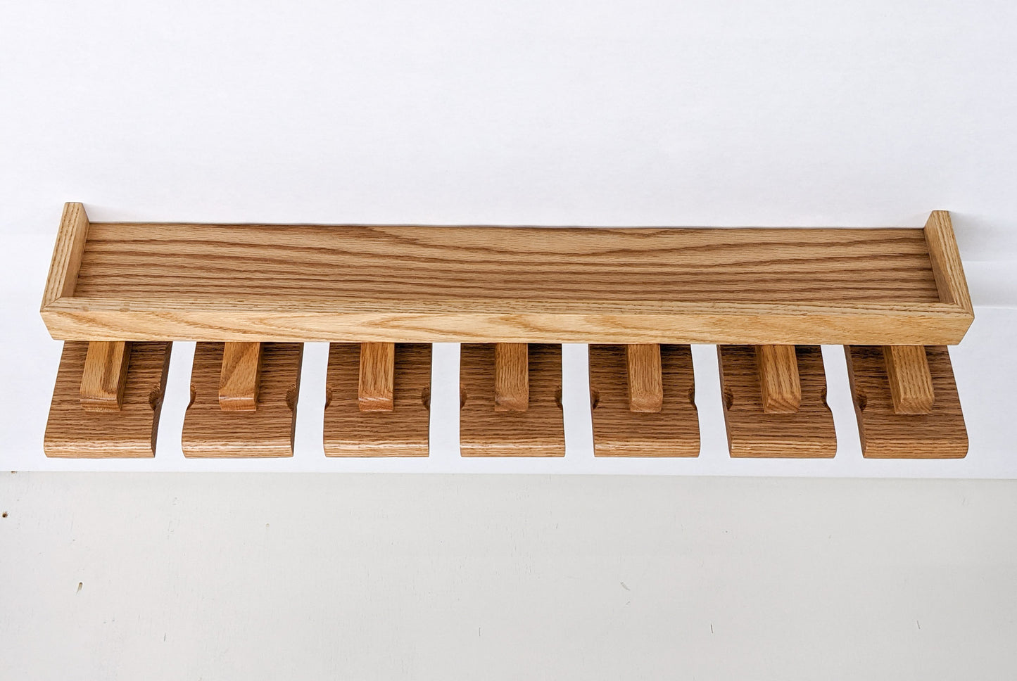 An empty beer glass shelf on a white background. The oak shelf has a small and long top with a raised edge while seven slats below allow for easy glass hanging. 