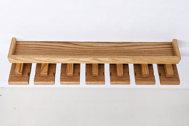 An empty beer glass shelf on a white background. The oak shelf has a small and long top with a raised edge while seven slats below allow for easy glass hanging.