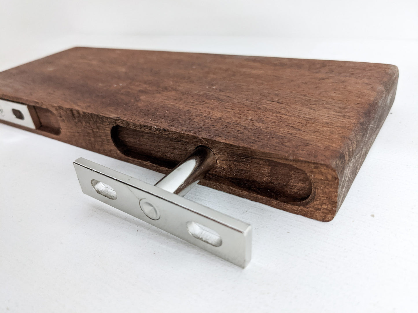 floating shelf with wall bracketsThe back of a medium floating shelf in mahogany demonstrating how two silver brackets and screws attach the shelf to the wall to make it appear as if it is floating.