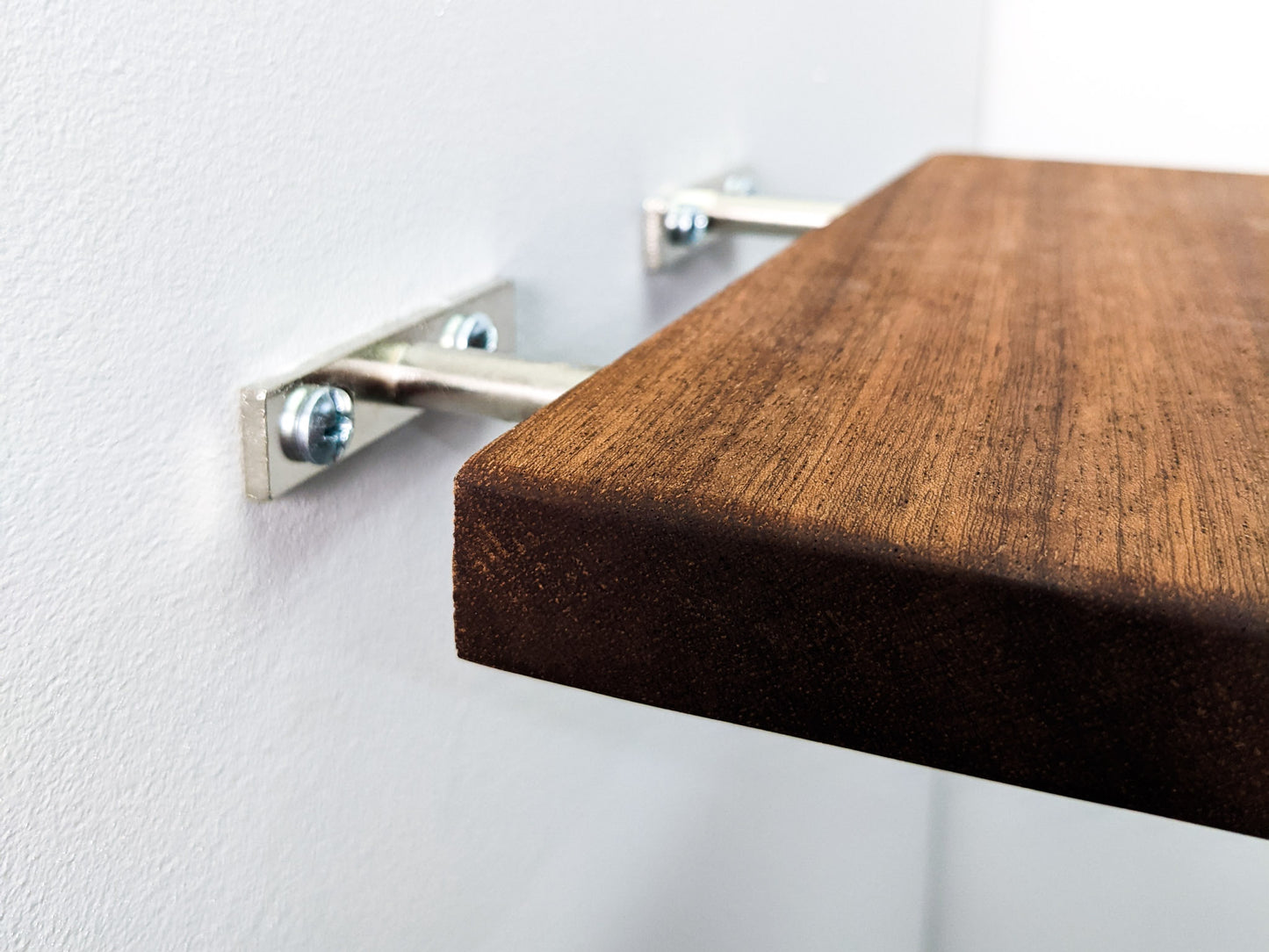 A medium mahogany floating shelf in the process of being installed. The brown wood shelf slides onto two secure silver brackets.