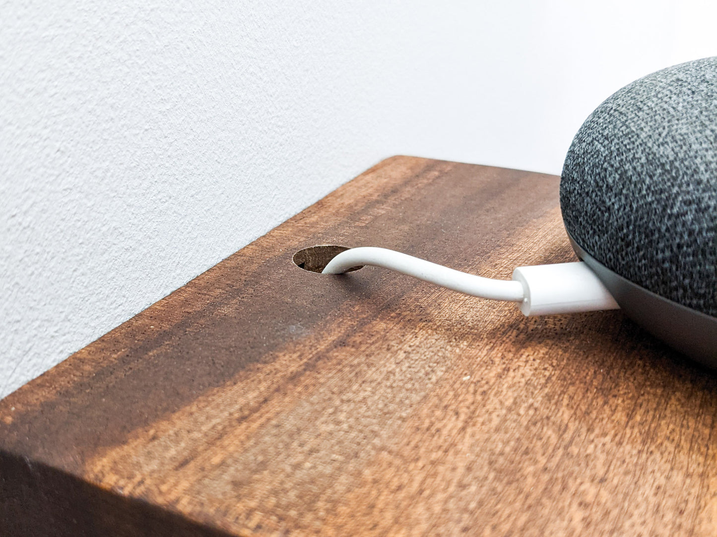 A close up of a white speaker cord that has been effortlessly threated through a clean small drilled hole in the back of a mahogany square shelf.