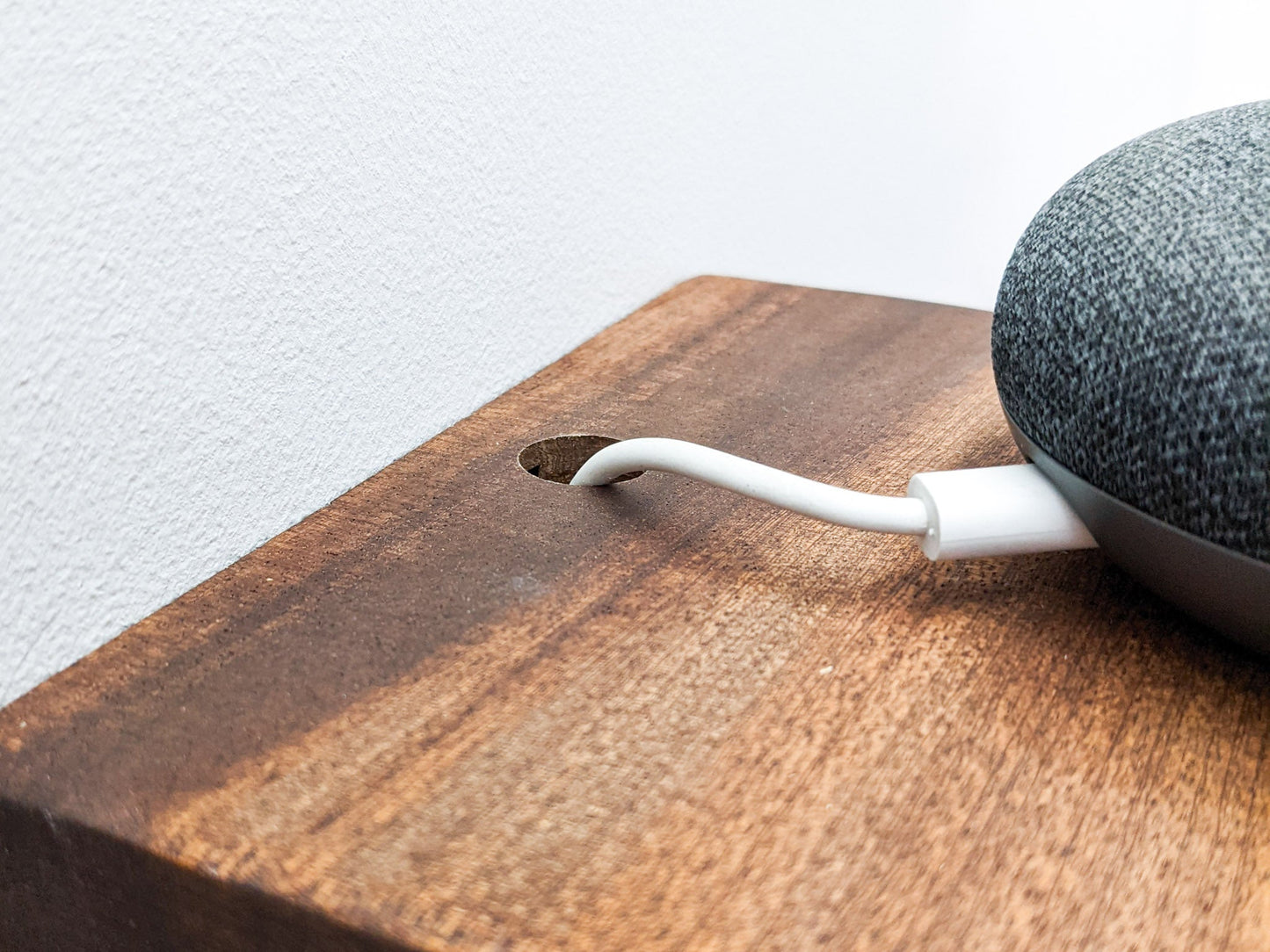 A close up of a white speaker cord that has been effortlessly threaded through a clean small drilled hole in the back of a mahogany square shelf.