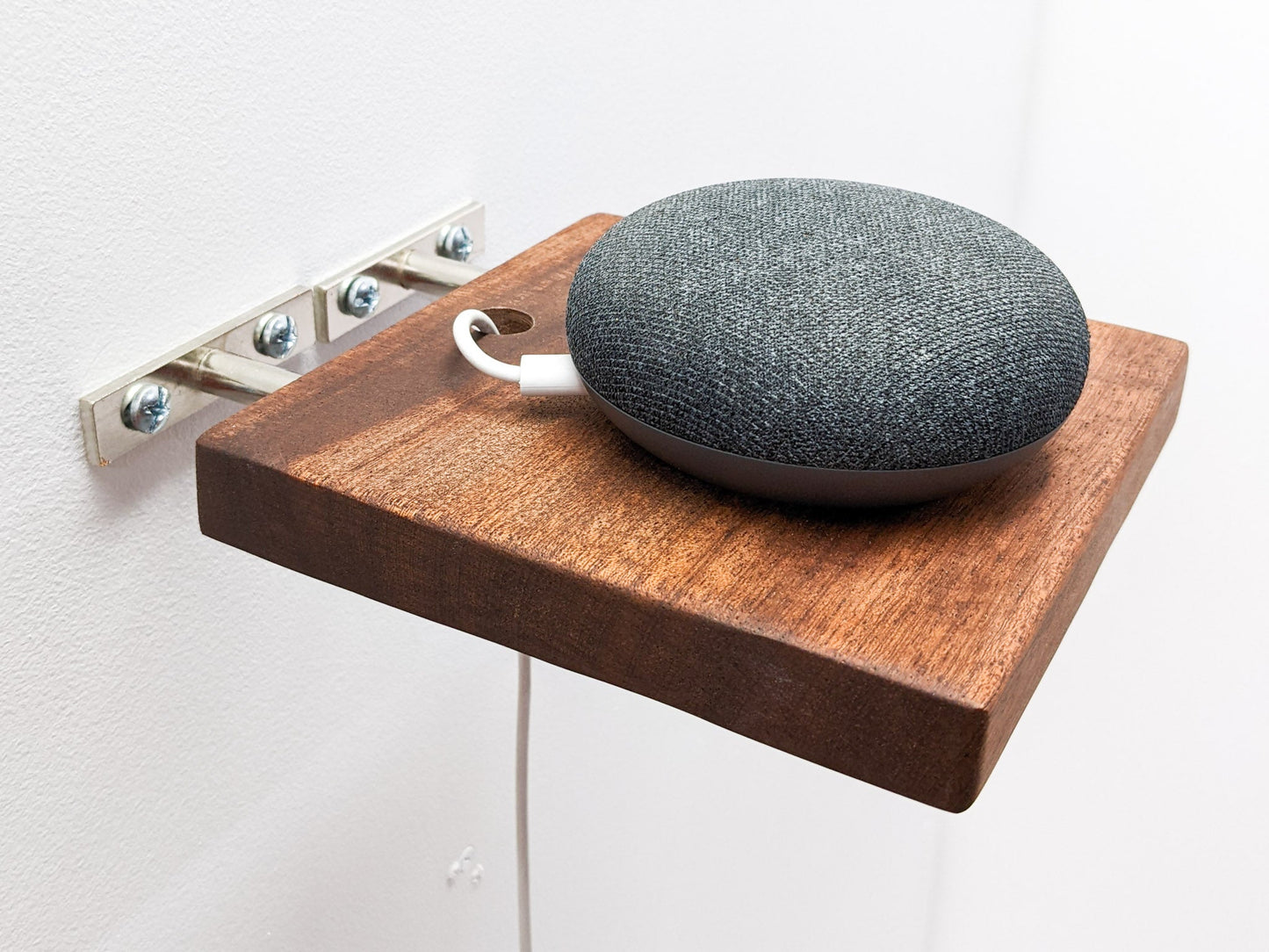 A small round speaker sits on top of a small mahogany square floating shelf that is mid-installation. A wire is plugged into the speaker and easily slips through a drilled hole in the shelf for easy and stylish cord management.