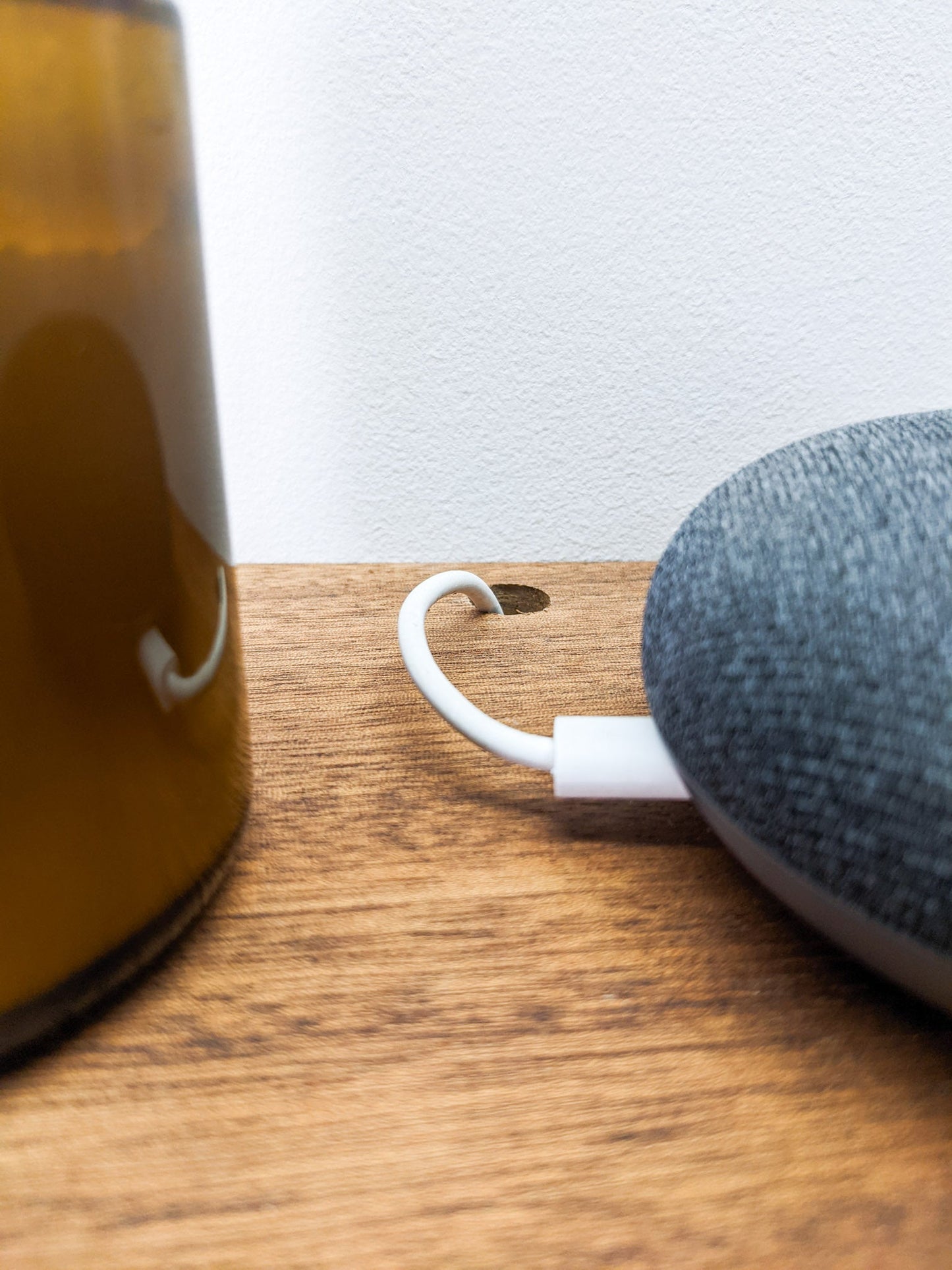 A close up view of a small hole that has been drilled in the back of our floating shelves to allow for seamless cord management. The speaker is half in the frame and sits to the right, a candle, more than half out of the frame, sits to the left.