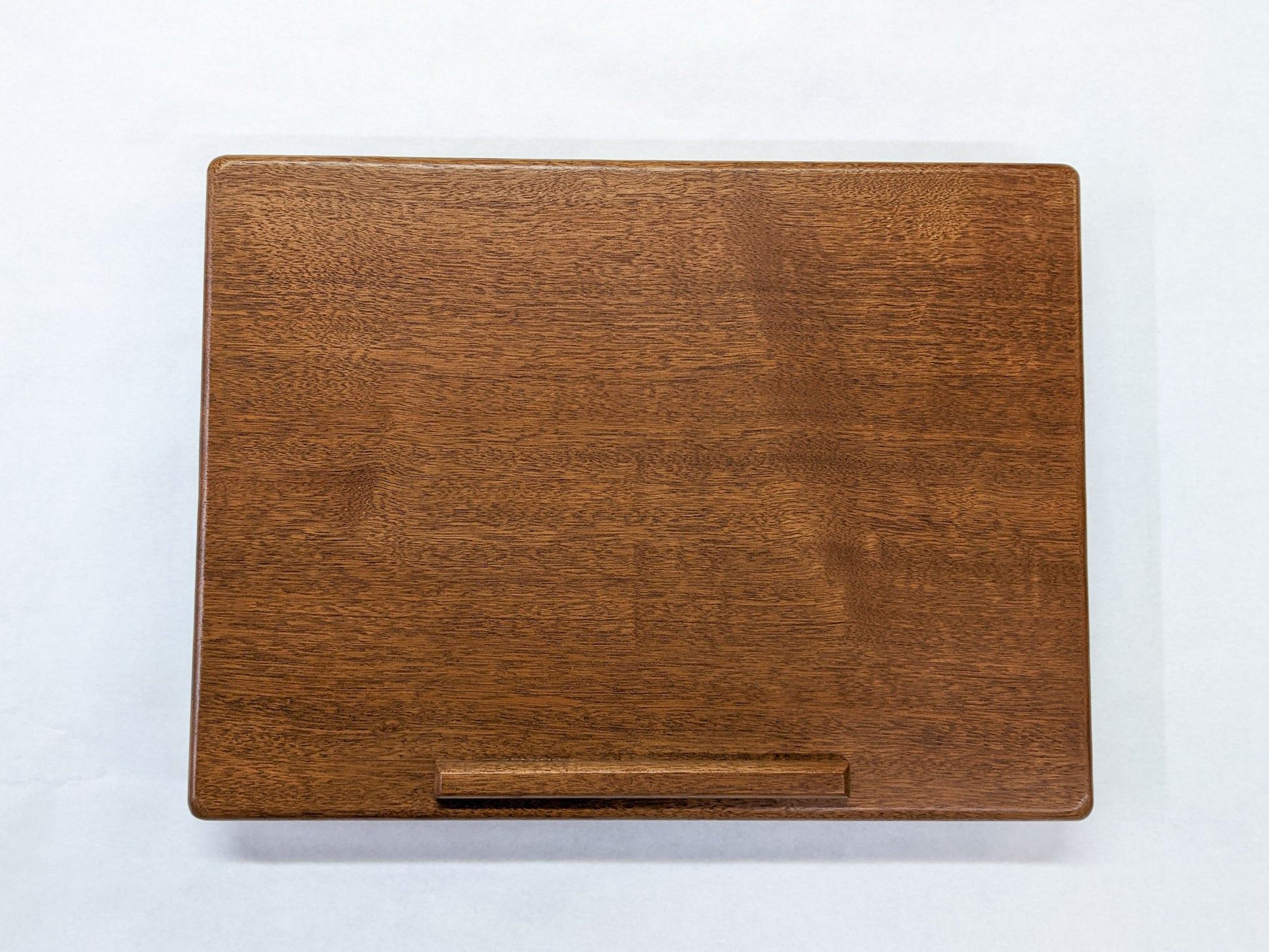 The surface of our Mahogany Leather Cushion Lap Desk. The mahogany wood is rich and the edges of the desk are soft and rounded. A protruding lip provides a stylish way to rest books or laptops.