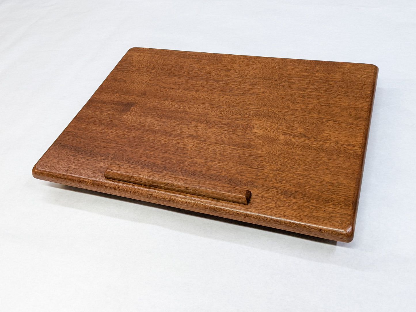 The surface of our Mahogany Leather Cushion Lap Desk. The mahogany wood is rich and the edges of the desk are soft and rounded. A protruding lip provides a stylish way to rest books or laptops.