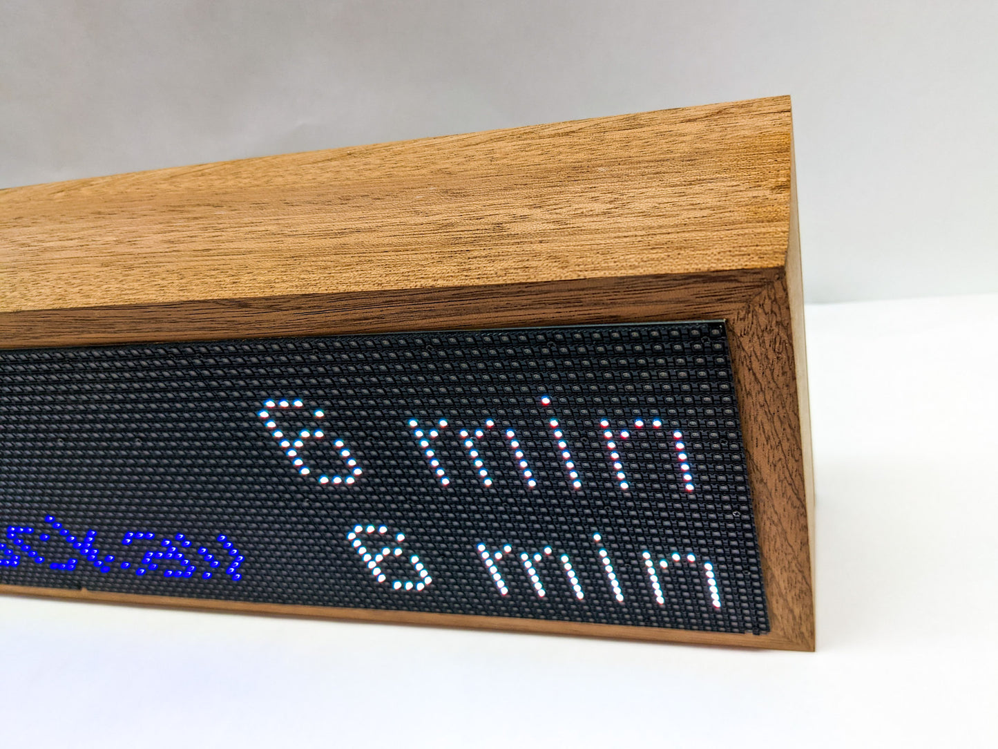A top-view of the mahogany frame on the top of the NYC subway clock. THe mahogany is thick and angular with interesting darker streaks of wood grain. A black LED screen meets the wood, on it is a white number 6 followed by min and repeated below it.