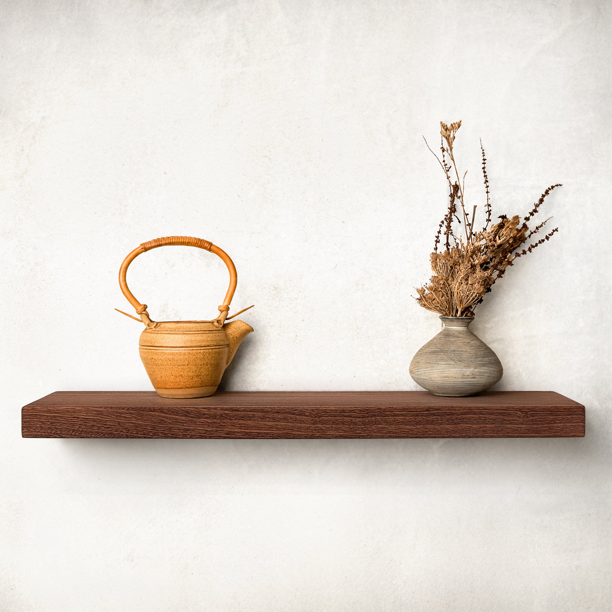 A long mahogany shelf is on a white wall with a pot and vase.