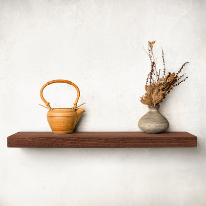 A long mahogany shelf is on a white wall with a pot and vase.