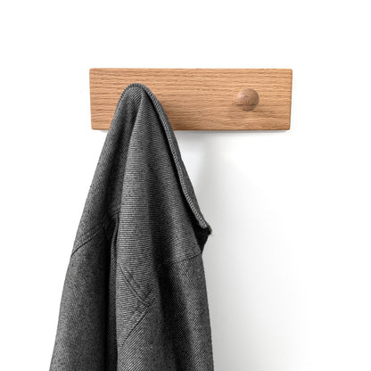 Two peg wooden wall hook with a gray coat hanging on it against a white background