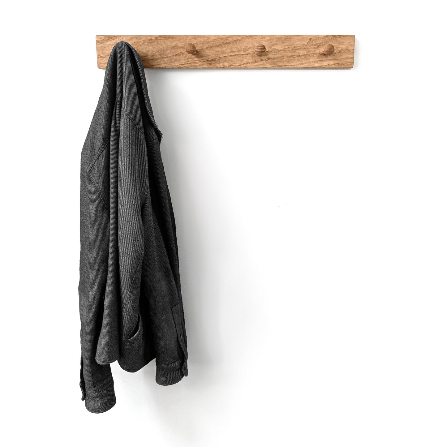 Gray coat hanging on a wooden wall hook against a white background