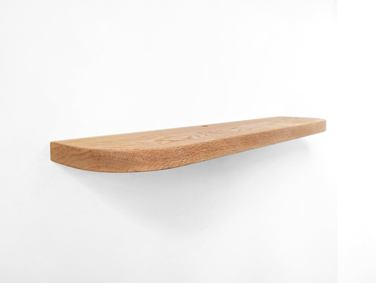 Angled photo of a long oak floating shelf with rounded edges and a cord hole