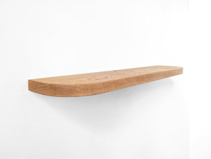 Angled photo of a long oak floating shelf with rounded edges and a cord hole