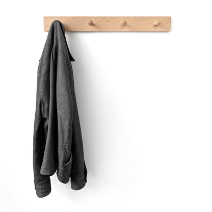 Gray jacket hanging on a wooden maple wall hook coat rack with four pegs against a white background