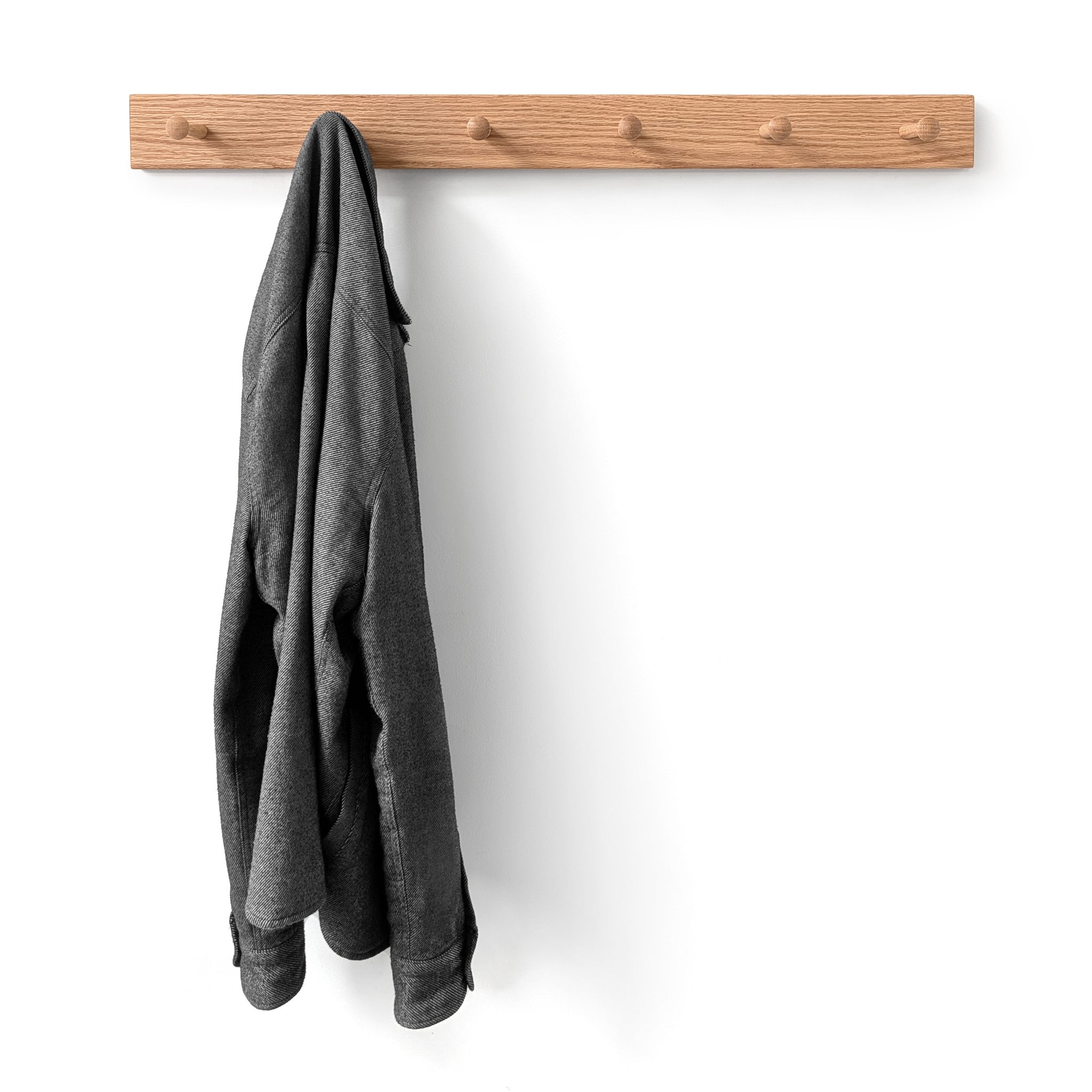 Gray jacket hanging on a six peg oak wooden peg rack against a white wall