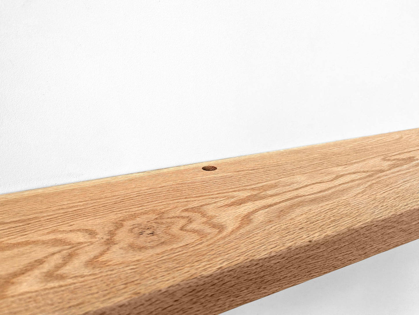 Zoomed in photo of a grommet hole in an oak floating shelf.