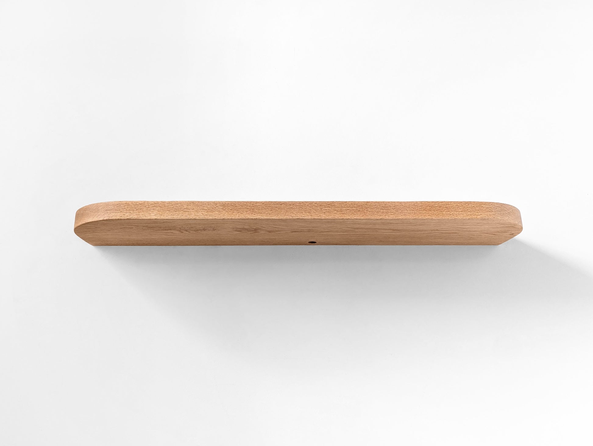 Photo from underneath of an oak floating shelf with curved edges and a grommet hole.