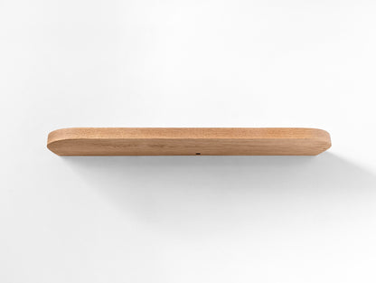 Photo from underneath of an oak floating shelf with curved edges and a grommet hole.
