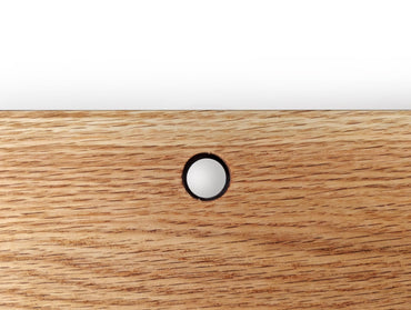 A cord hole in an oak shelf.
