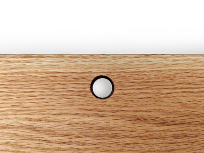 A cord hole in an oak shelf.