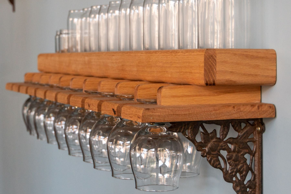 A beer glass shelf is on the wall with 16oz and 12oz beer glasses and tulip glasses