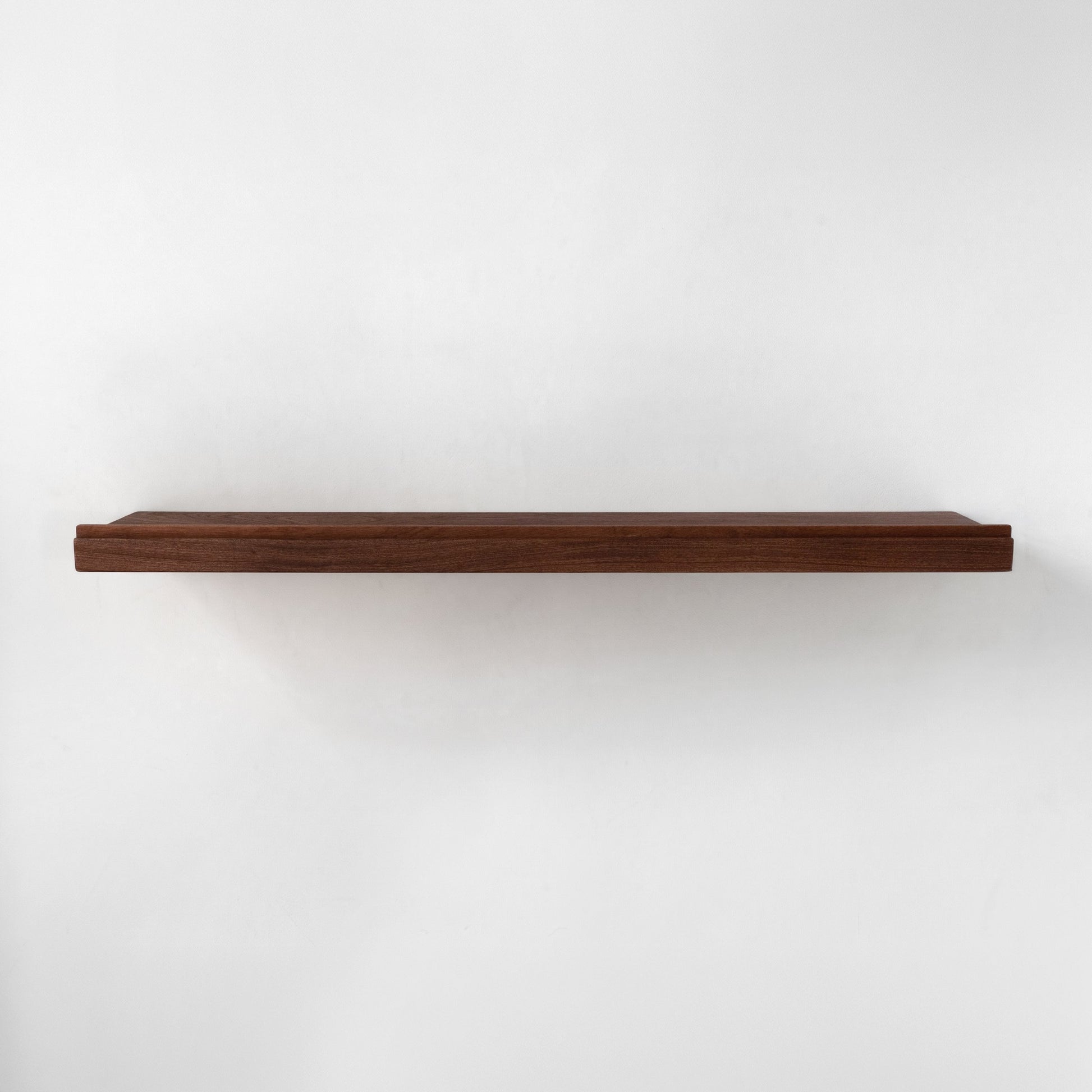 A single long floating shelf made of dark brown wood and a lip on the front, shown horizontally against a plain white wall.