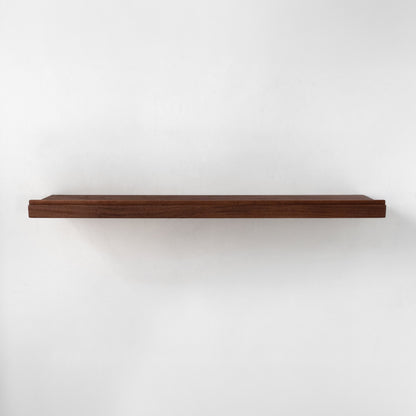 A single long floating shelf made of dark brown wood and a lip on the front, shown horizontally against a plain white wall.