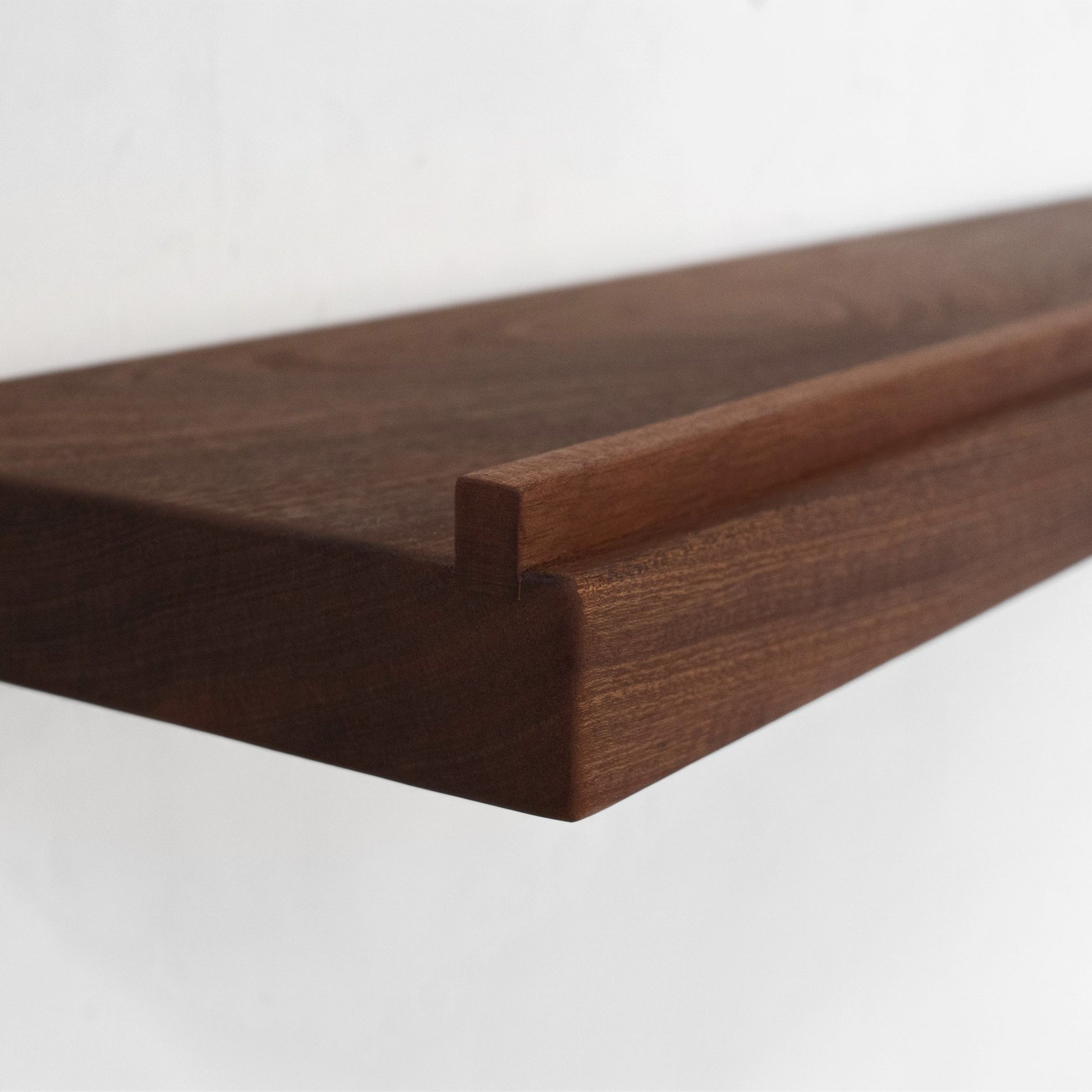 Close-up of a dark brown mahogany wooden floating shelf with a ledge on the front, showing the wood grain and corner joint against a plain white background.