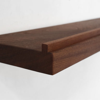 Close-up of a dark brown mahogany wooden floating shelf with a ledge on the front, showing the wood grain and corner joint against a plain white background.