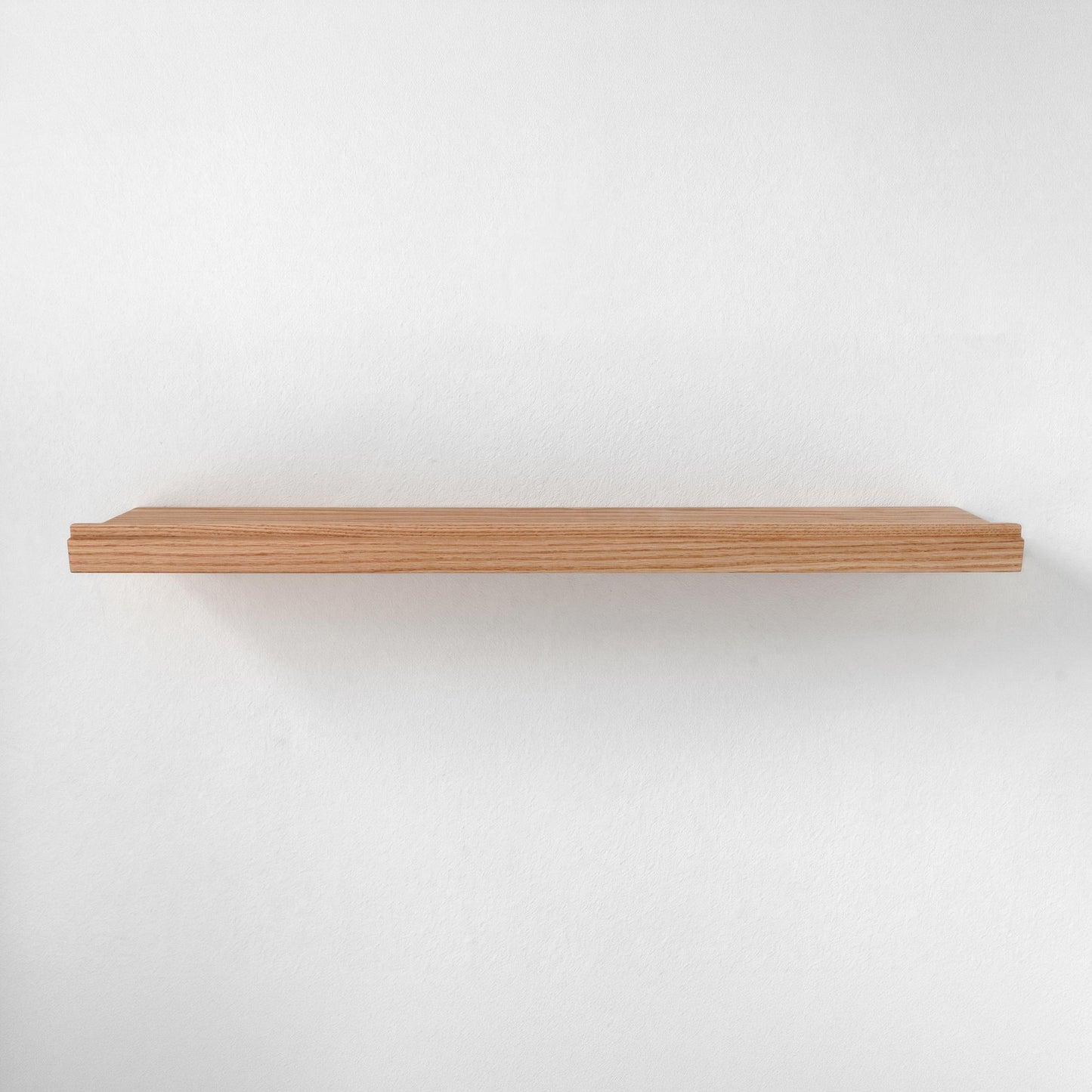 A single light brown wooden floating shelf with a smooth finish and rounded ends and ledge at the front edge, mounted against a plain white wall.
