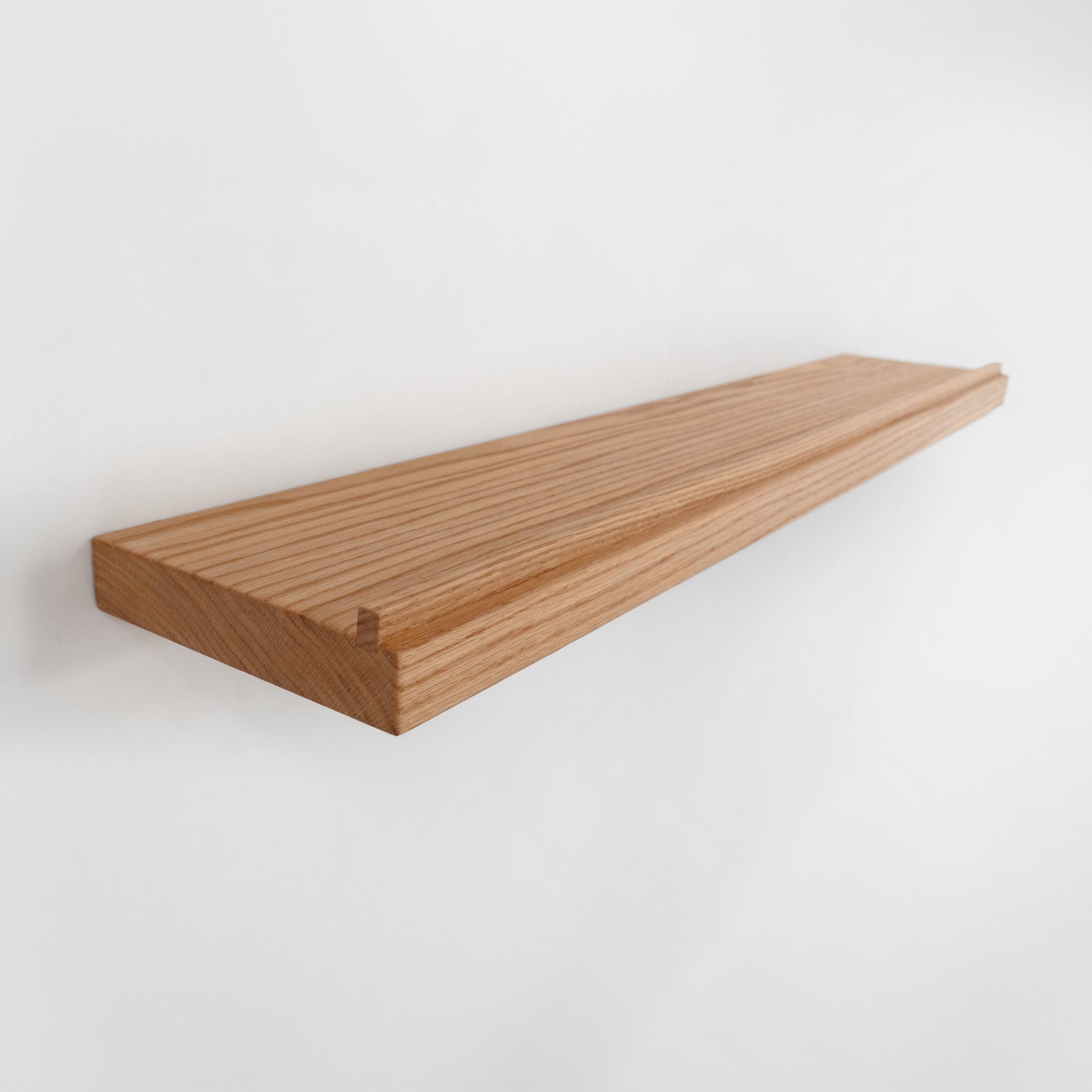 A long, narrow floating wooden shelf made of oak wood with visible grain, shown mounted against a plain white wall.
