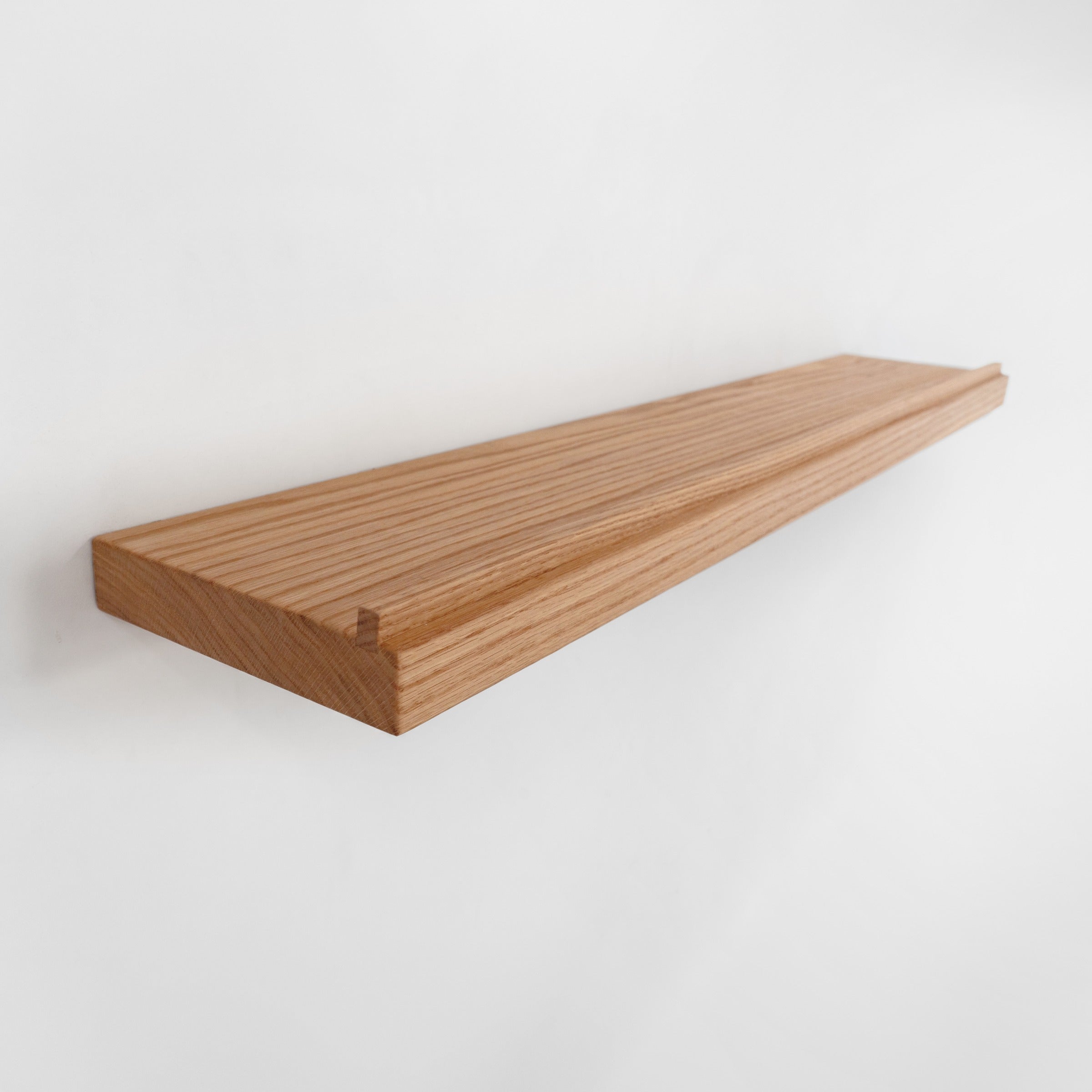 A long, narrow floating wooden shelf made of oak wood with visible grain, shown mounted against a plain white wall.