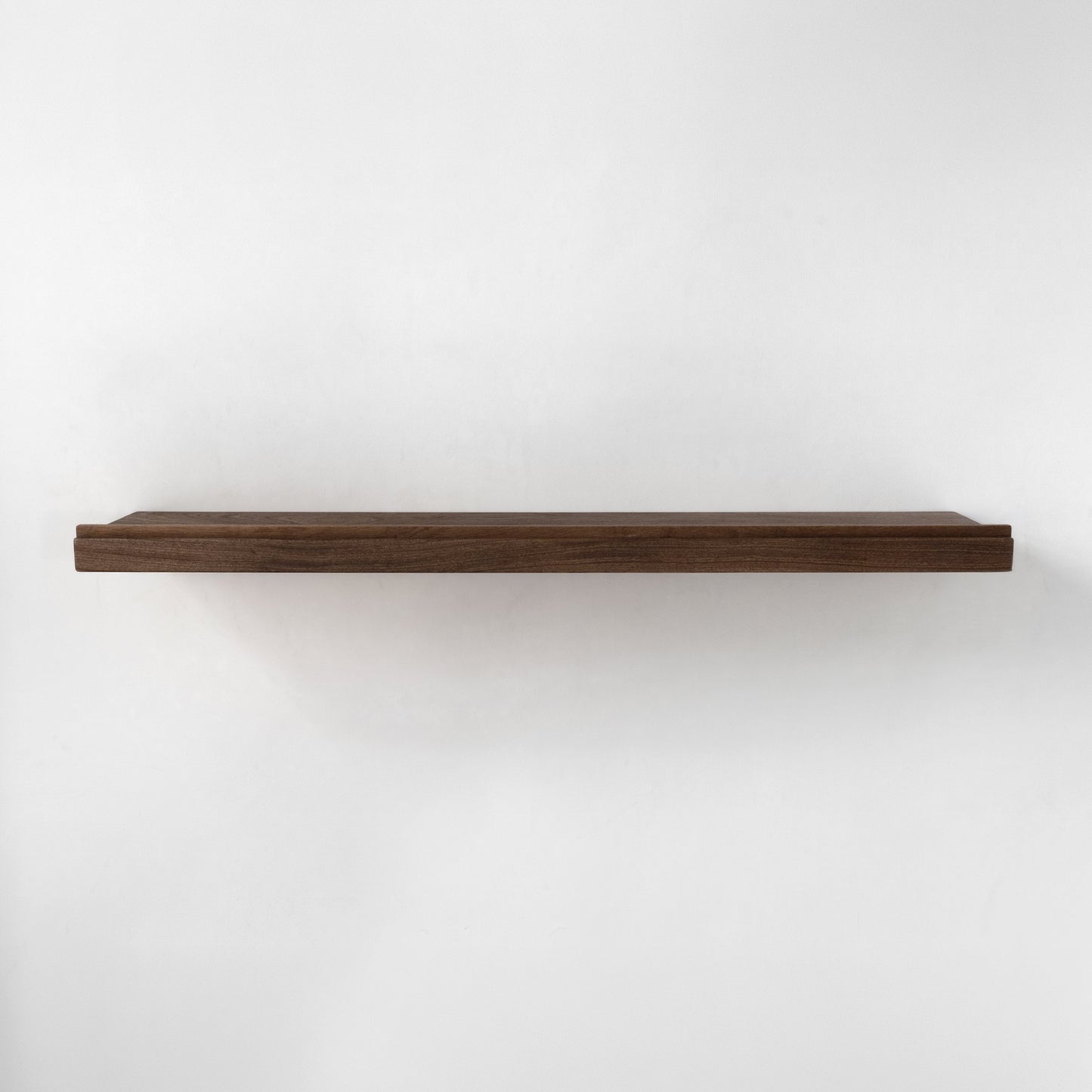 A single long floating wooden shelf with a rim in a dark brown finish, mounted against a plain white wall.