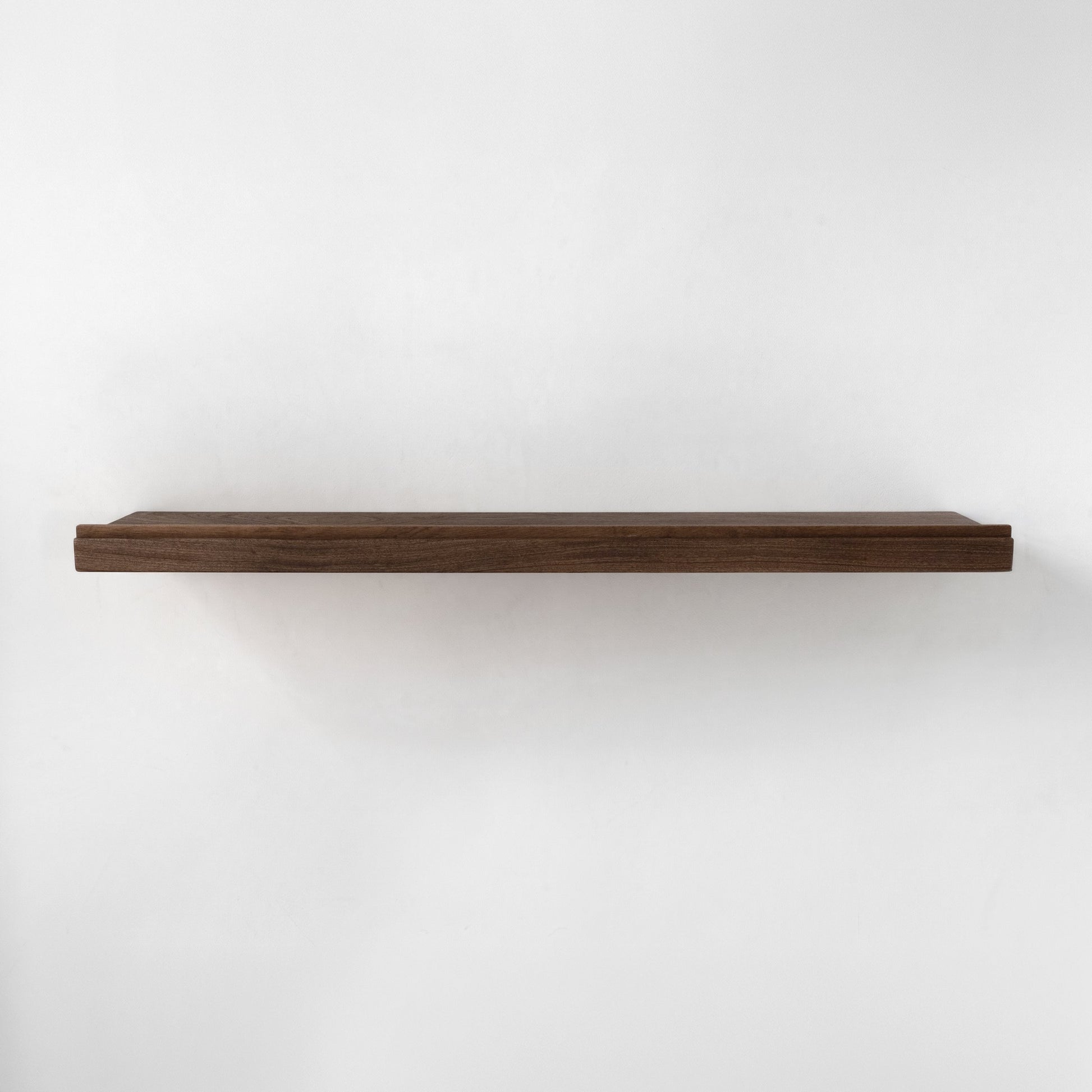 A single long floating wooden shelf with a rim in a dark brown finish, mounted against a plain white wall.