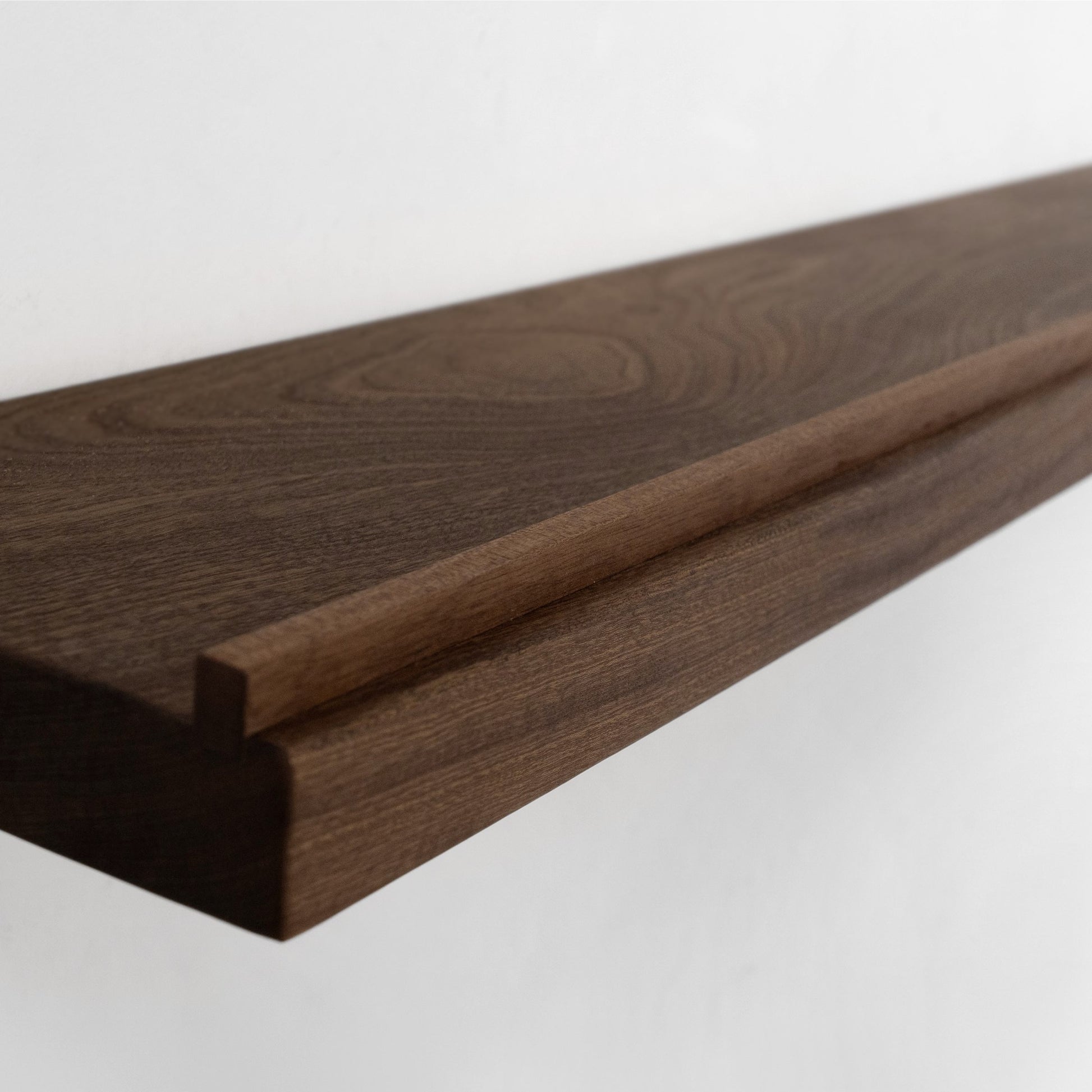 A close-up of a walnut floating shelf with a modern stepped profile and visible wood grain, shown against a plain white background.