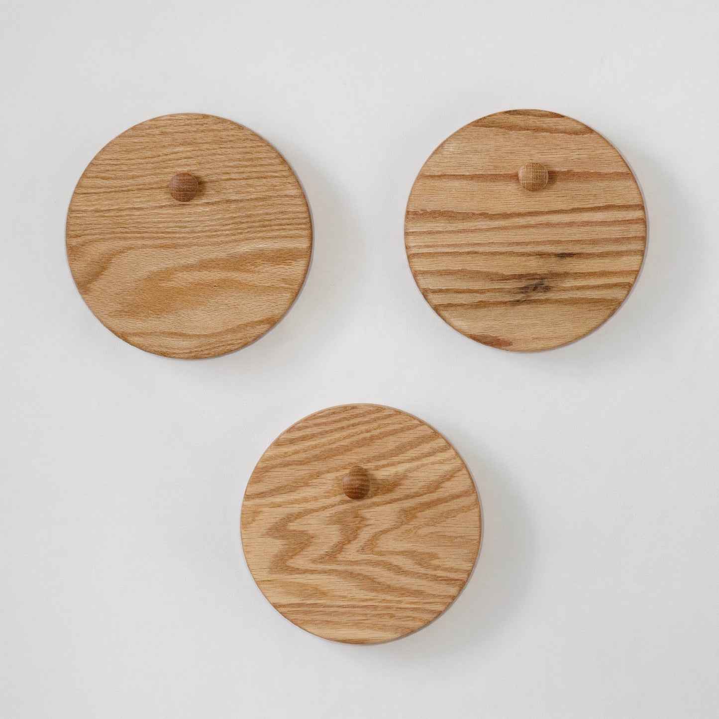 Three round oak wood wall hooks with small wooden pegs, arranged on a plain white background.