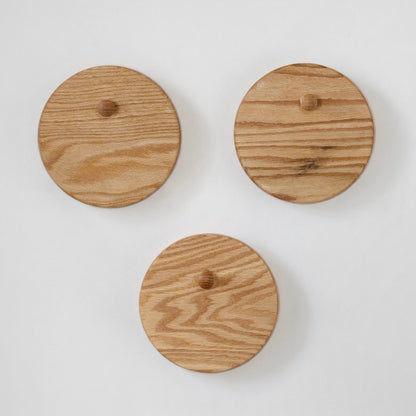 Three round oak wood wall hooks with small wooden pegs, arranged on a plain white background.