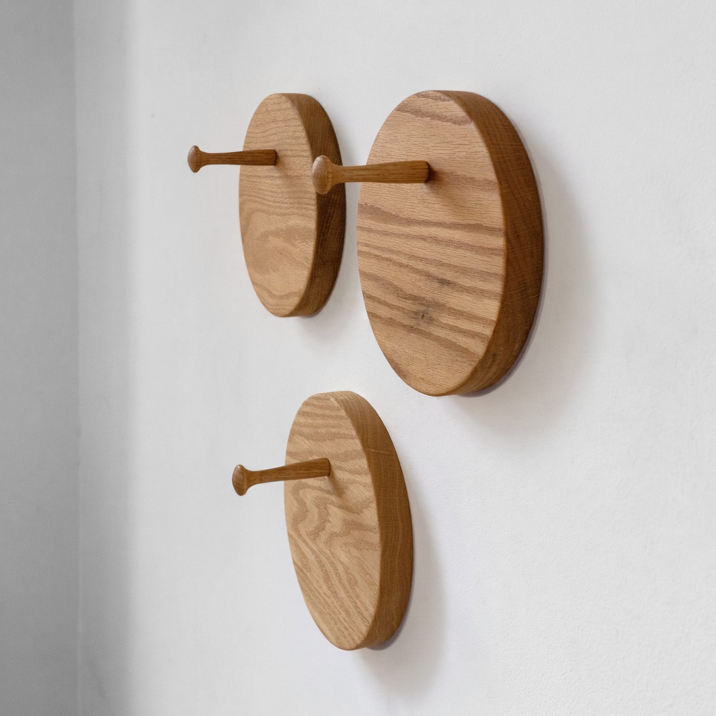 Three round wooden hat racks with natural oak grain, arranged diagonally on a plain white wall.