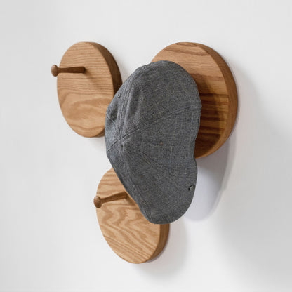 A gray flat cap hat hanging from one of three round wooden hat racks on a plain white wall.